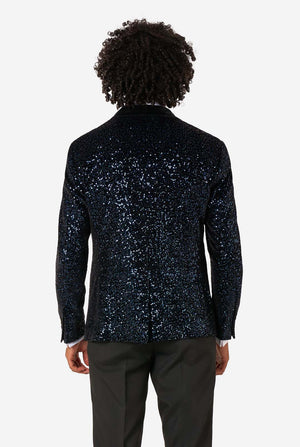 A man poses in a navy sequined blazer or dinner jacket, wearing a solid white shirt underneath. View from the back