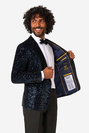 A man poses in a navy sequined blazer or dinner jacket, wearing a solid white shirt underneath. Showing the inside of the jacket