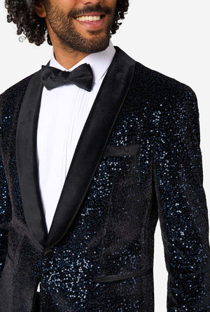 A man poses in a navy sequined blazer or dinner jacket, wearing a solid white shirt underneath. Close up of the chest
