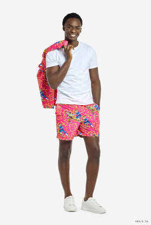 Man wearing pink summer set consisting of shirts and shorts. Summer set has Dragon Ball Z Goku and Vegeta fighting print. Holding the shirt over his shoulder and wearing white T-shirt.