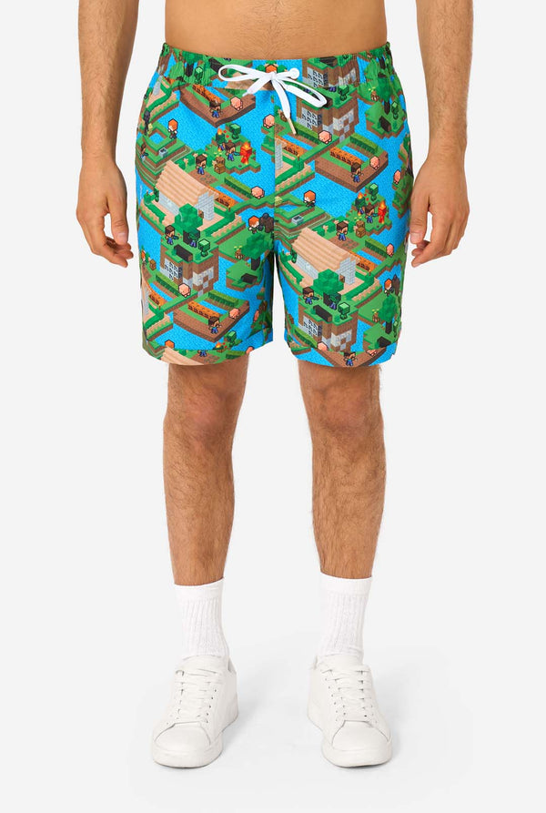 A man wearing a colorful summer outfit featuring a Minecraft Overworld print, showcasing pixelated landscapes, characters, and elements from the iconic game. The short-sleeve shirt and matching shorts highlight a vibrant design inspired by the Minecraft universe. Close-up shorts