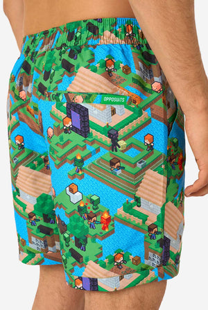 A man wearing a colorful summer outfit featuring a Minecraft Overworld print, showcasing pixelated landscapes, characters, and elements from the iconic game. The short-sleeve shirt and matching shorts highlight a vibrant design inspired by the Minecraft universe. Close-up shorts from the back