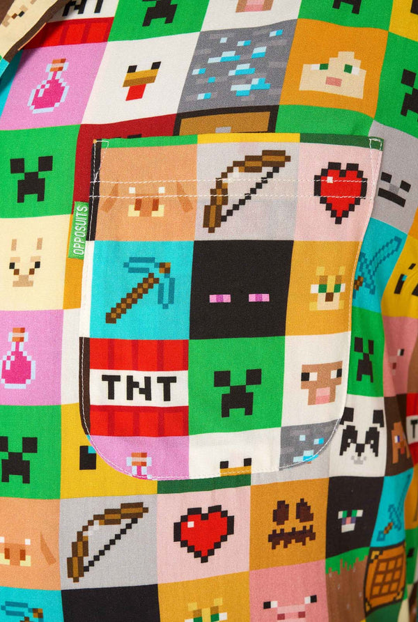 Man wearing a colorful Minecraft Hawaiian shirt featuring pixelated blocks, characters, and items from the game, paired with black pants, standing against a plain white background. Close up of the chest pocket
