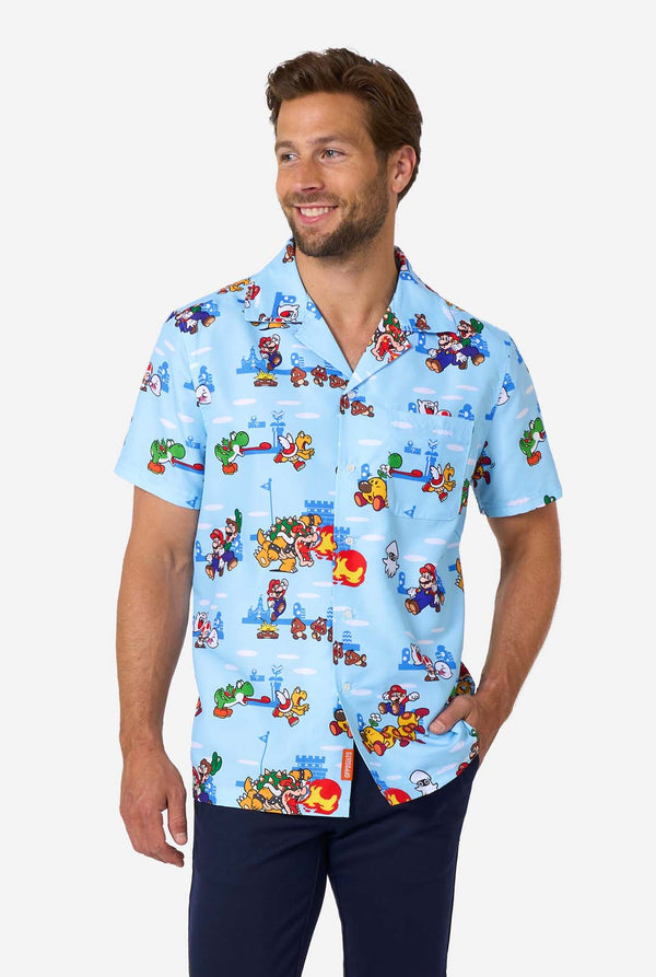 A man smiles while wearing a light blue, short-sleeved Hawaiian-style shirt printed all over with various scenes and characters from the Super Mario video game series.