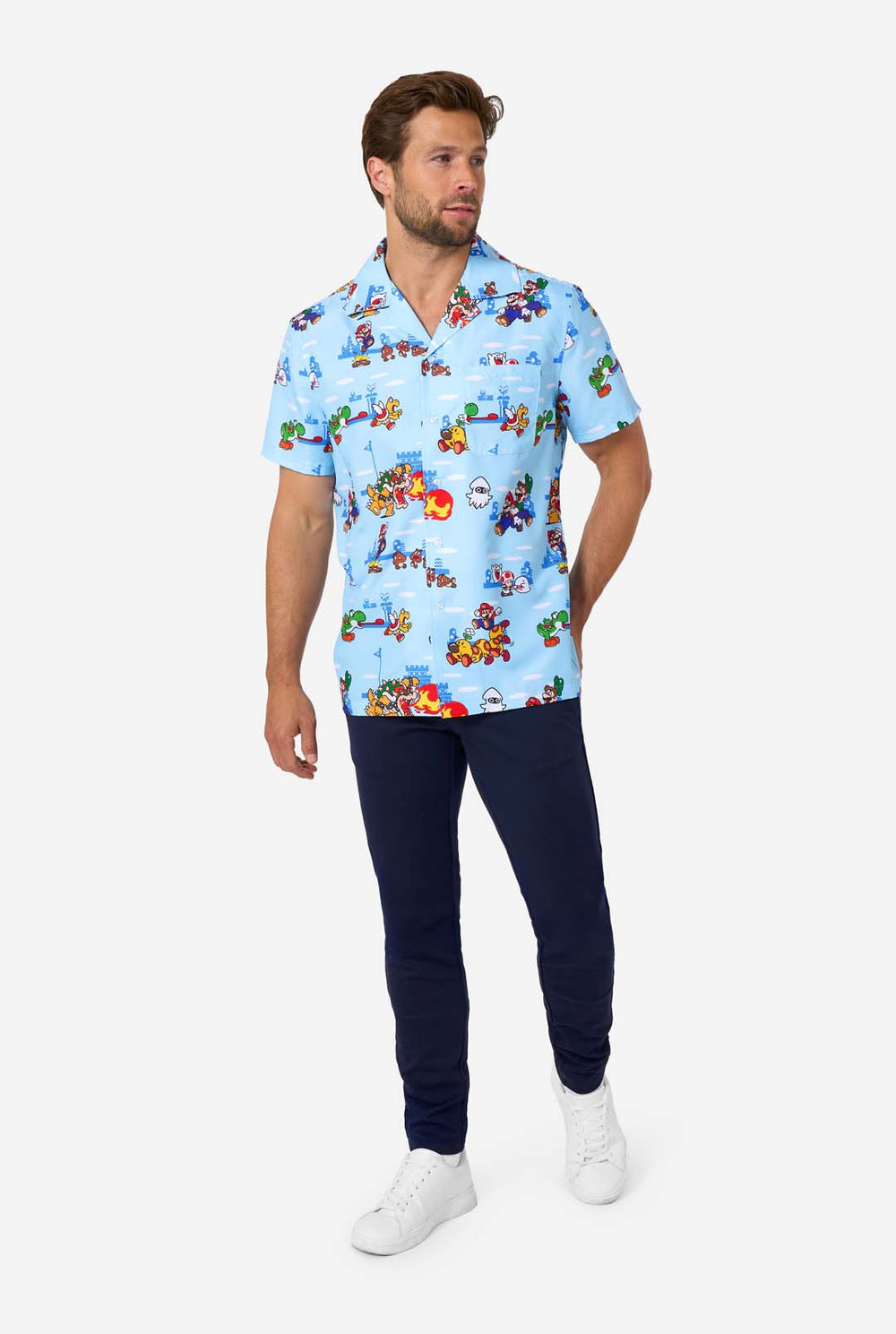 A man smiles while wearing a light blue, short-sleeved Hawaiian-style shirt printed all over with various scenes and characters from the Super Mario video game series.