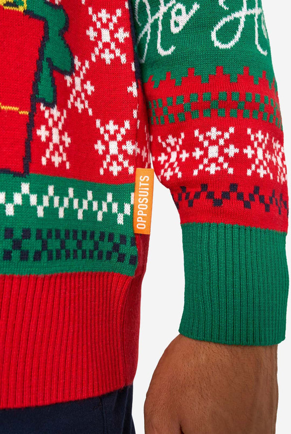 Smiling man wearing a colorful knitted Christmas sweater featuring Santa Claus, Rudolph, and the text “So Jolly.” Sleeve close-up.