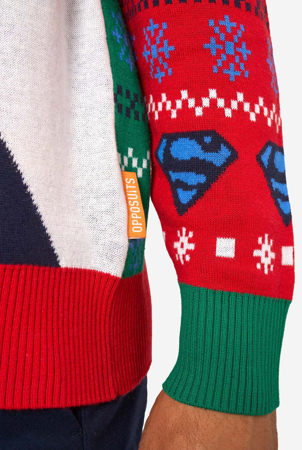 Man wearing a colorful knitted Christmas sweater featuring multiple Superman designs and the iconic “S” logo. Sleeve close-up.