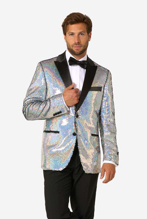 Man wearing a holographic silver sequin tuxedo with black satin lapels, paired with a white shirt, black bow tie, and black trousers, standing with one hand adjusting the jacket.