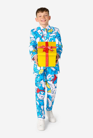 Teen boy wearing a vibrant Smurfs kids suit with colorful cartoon character prints in blue, red, yellow, and white, paired with a matching tie and white shirt, smiling against a plain background. Holding a present.