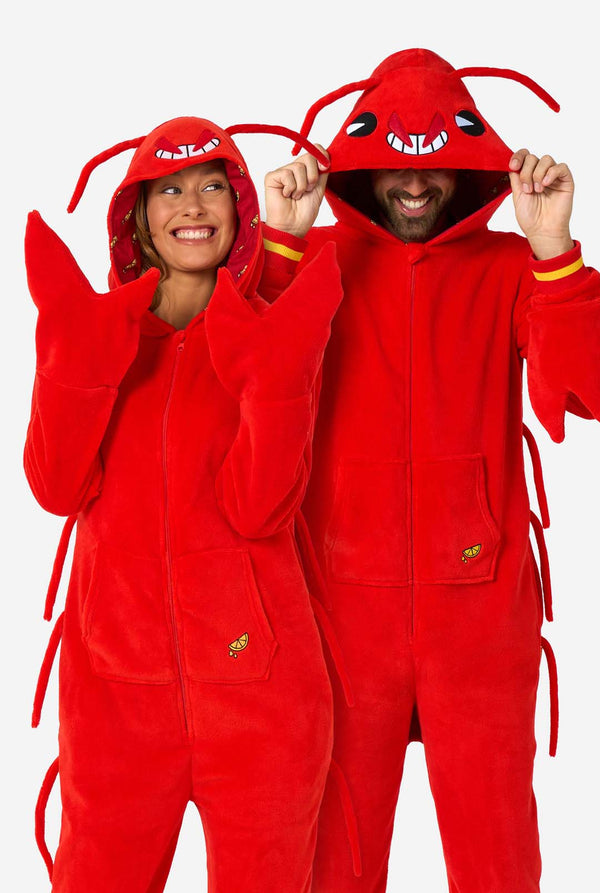 A man and women are wearing a bright red lobster-themed adult onesie featuring playful hood details and cozy, soft material, perfect for lounging or costume events. including stitched gloves as claws. Both are wearing their hood on their heads.