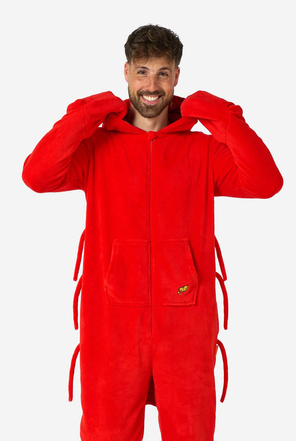 A man is wearing a bright red lobster-themed adult onesie featuring playful hood details and cozy, soft material, perfect for lounging or costume events. including stitched gloves as claws. Hood is down on his back.