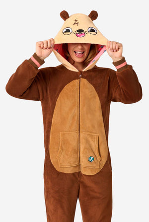A smiling woman is wearing a brown adult onesie designed as an otter. The onesie features a hood with ears, a cute face, and playful otter details, perfect for cozy lounging or costume parties. 