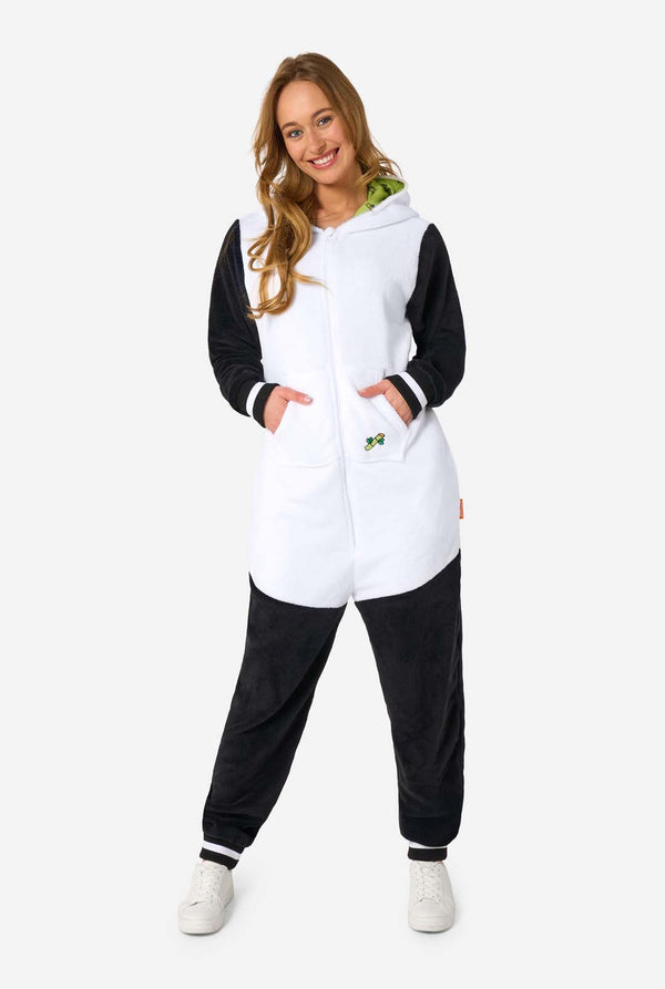 A woman is wearing a panda-themed adult onesie. This cozy onesie features black and white panda colors with a playful hood showcasing panda ears and a cute face. Perfect for lounging or fun costume occasions. 