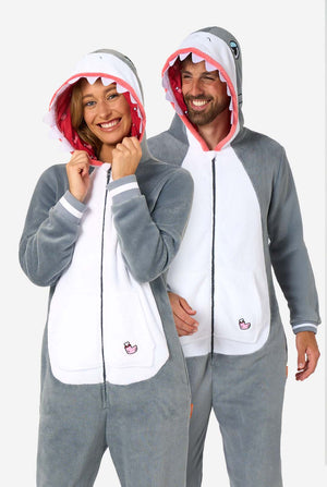 A man and women are wearing a grey and white shark adult onesie featuring playful hood details and cozy, soft material, perfect for lounging or costume events. Both are wearing their hoods on their head.