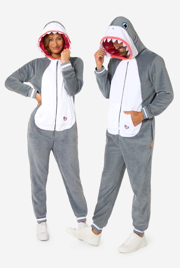 A man and women are wearing a grey and white shark adult onesie featuring playful hood details and cozy, soft material, perfect for lounging or costume events. Both are wearing their hoods on their head. Full body image.
