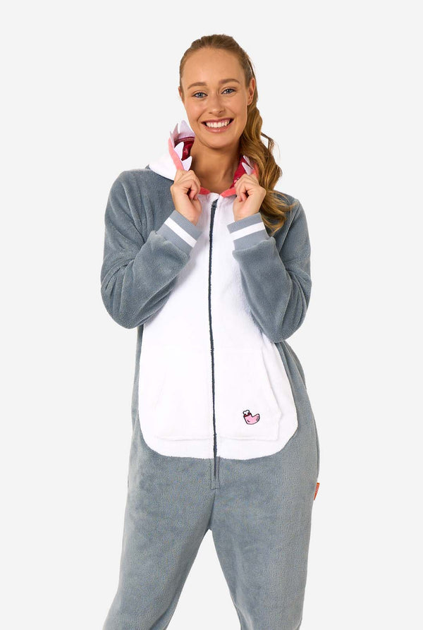 A women is wearing a grey and white shark adult onesie featuring playful hood details and cozy, soft material, perfect for lounging or costume events. Her hood is on her back.