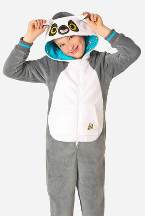 Child wearing a cozy unisex kids onesie designed as a lemur, featuring grey and white plush fabric, a hood with a cartoon lemur face and ears, and a playful banana print on the pocket.