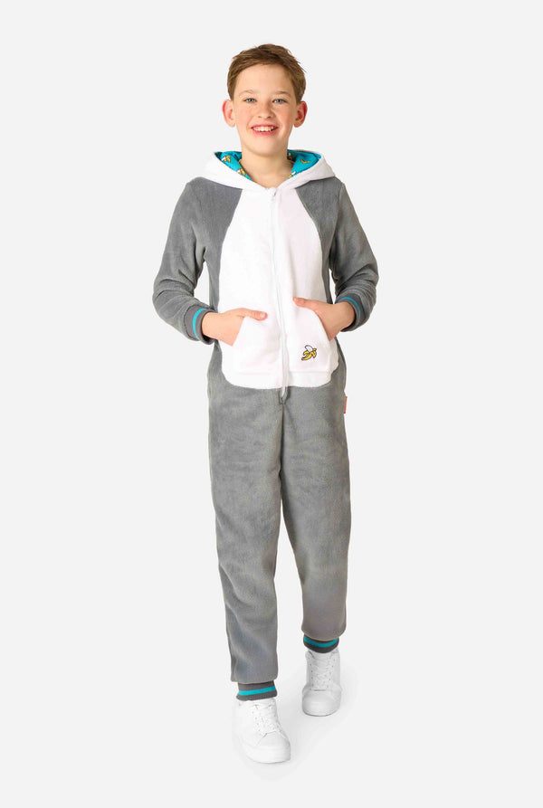 Child wearing a cozy unisex kids onesie designed as a lemur, featuring grey and white plush fabric, a hood with a cartoon lemur face and ears, and a playful banana print on the pocket. Full body.