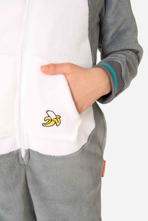 Child wearing a cozy unisex kids onesie designed as a lemur, featuring grey and white plush fabric, a hood with a cartoon lemur face and ears, and a playful banana print on the pocket. Focused on a hand inside a pocket.