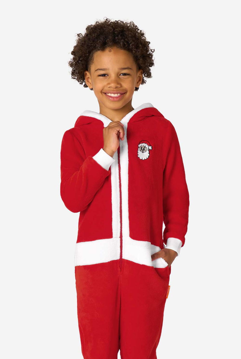 Child wearing a red Santa-themed onesie with a white-trimmed hood, standing angled to the side with hands in the pockets.