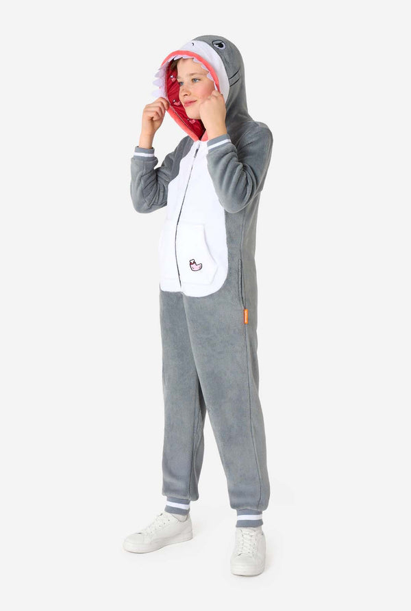 Side view of a smiling child in a grey shark onesie with white belly and red-lined hood, holding the hood slightly open to reveal the face.