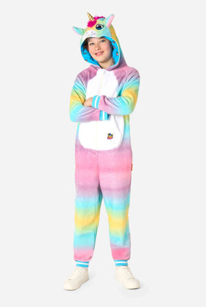 A smiling kid is wearing a white, pink, blue and yellow kids onesie designed as a unicorn. The Unicorn onesie features a hood resembling a unicorn head and other playfull details. Full body image.