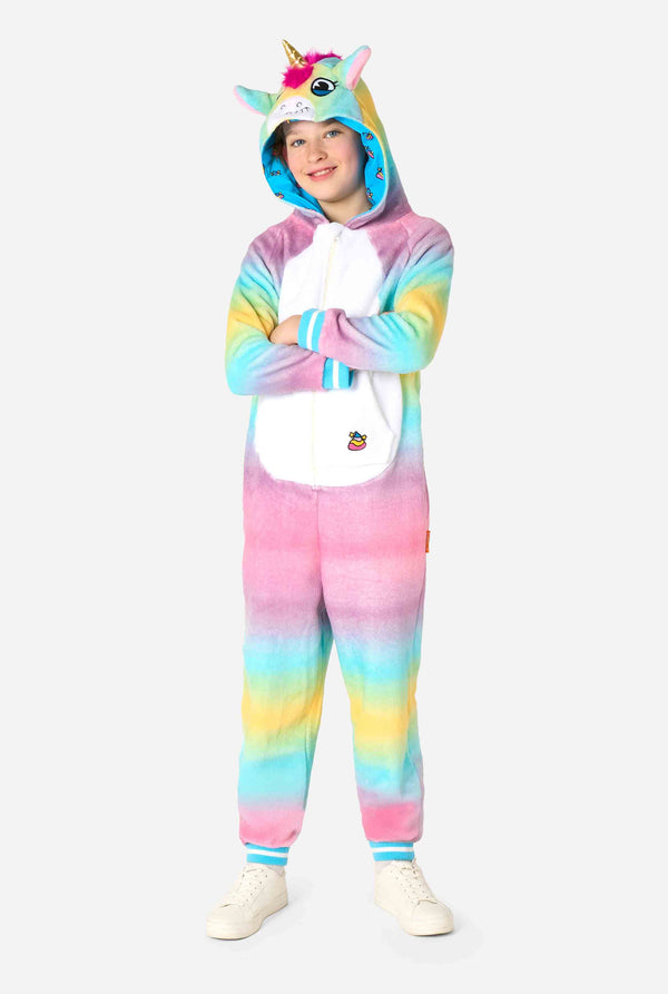 A smiling kid is wearing a white, pink, blue and yellow kids onesie designed as a unicorn. The Unicorn onesie features a hood resembling a unicorn head and other playfull details. Full body image.