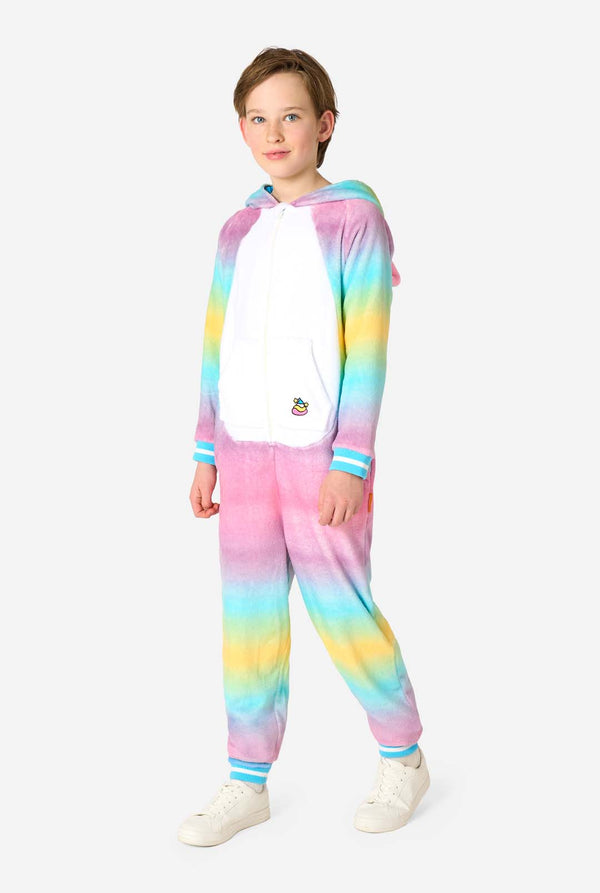 A child stands modeling a soft, hooded unicorn onesie that features a bright, pastel rainbow color gradient on the arms and legs and a white front panel.