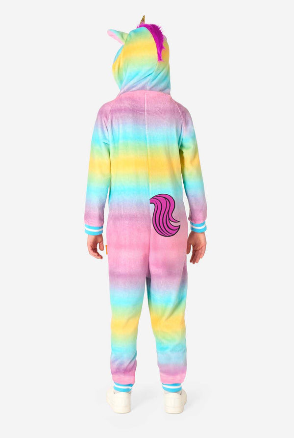 A child stands modeling a soft, hooded unicorn onesie that features a bright, pastel rainbow color gradient on the arms and legs and a white front panel. View from the back