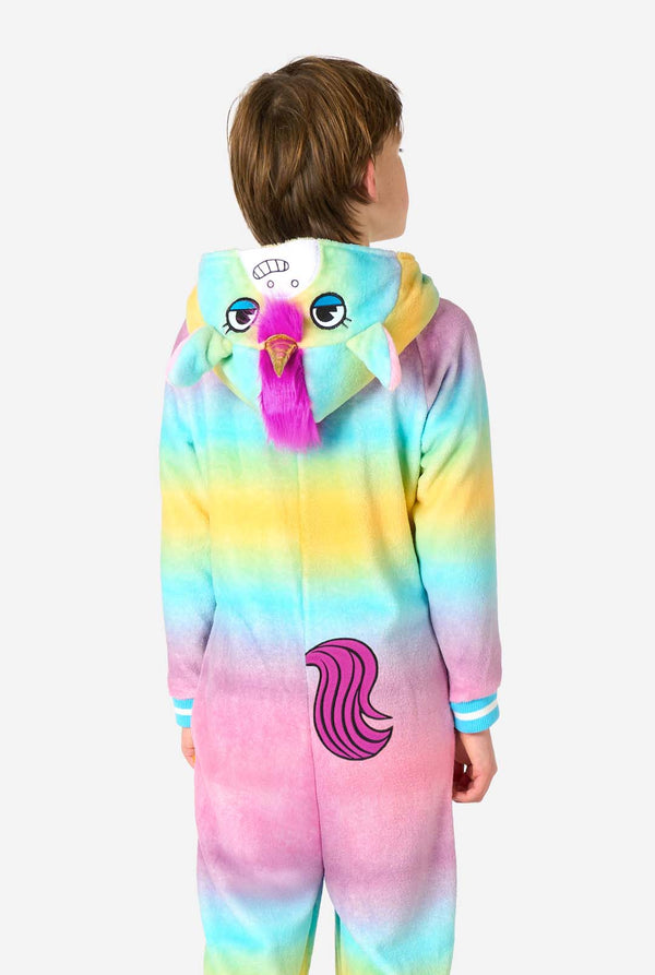 A child stands modeling a soft, hooded unicorn onesie that features a bright, pastel rainbow color gradient on the arms and legs and a white front panel. View from the back