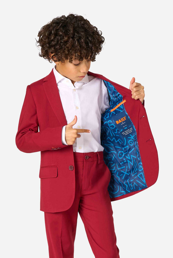 Kid wearing a stylish burgundy red suit with a white dress shirt, looking confidently. Perfect formal outfit for boys' special occasions, weddings, and parties. Holding one side of the jacket open.