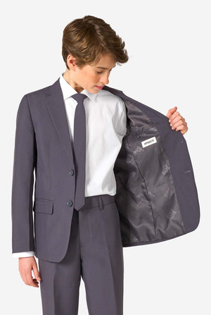 Teen boy wearing a stylish charcoal colored grey suit with a white dress shirt, smiling confidently. Perfect formal outfit for boys' special occasions, weddings, and parties. Holding one side of his jacket open.