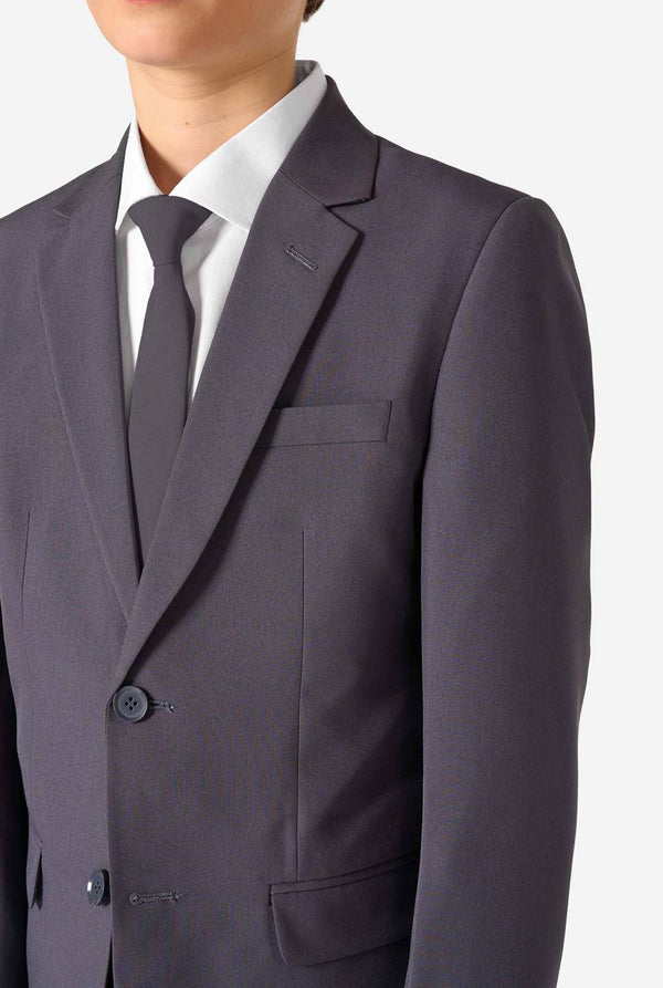Teen boy wearing a stylish charcoal colored grey suit with a white dress shirt, smiling confidently. Perfect formal outfit for boys' special occasions, weddings, and parties. Chest close-up.